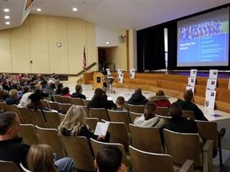 Wide angle view of auditorium full of people watching a presenter speak