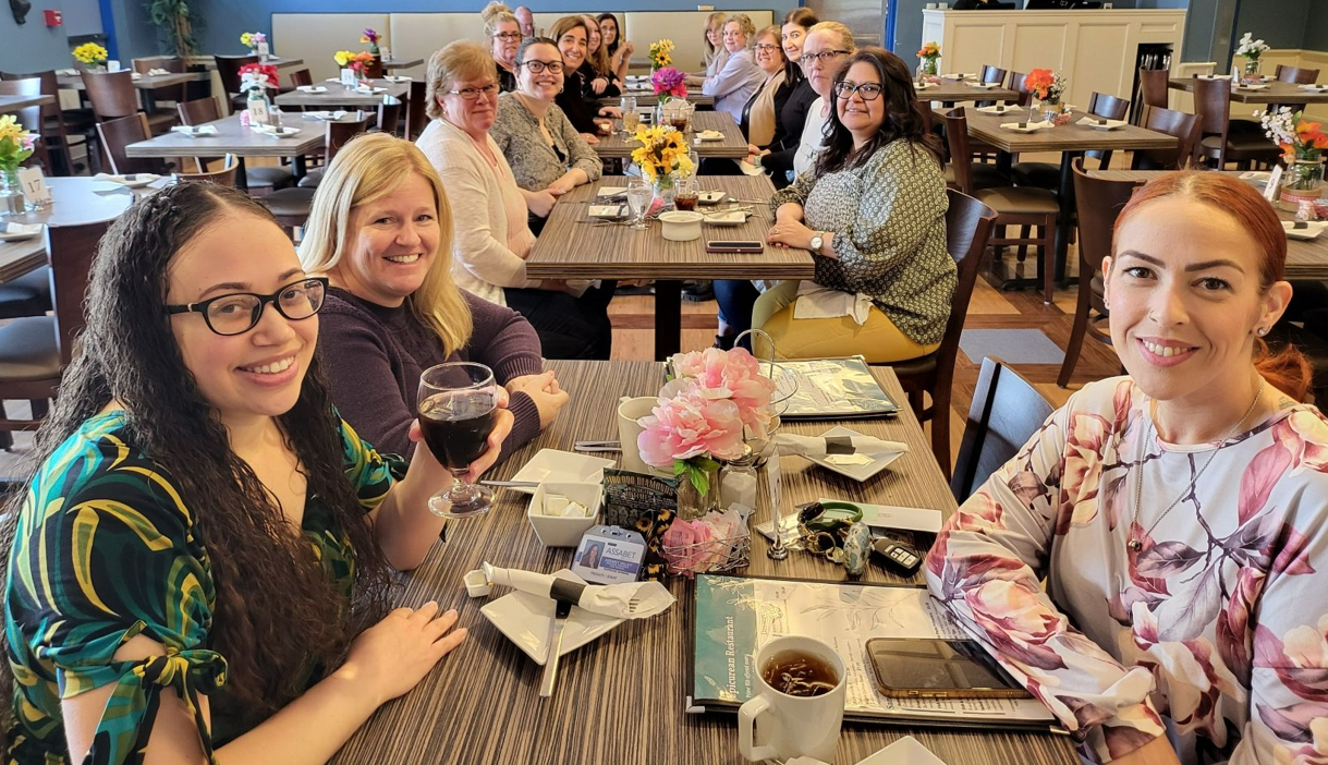 Business' office staff smiling and sitting around flowers and menus in the school's Epi