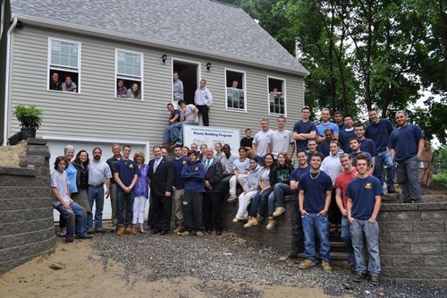 Staff and students posing for a large group photo from a distance in front of a community project