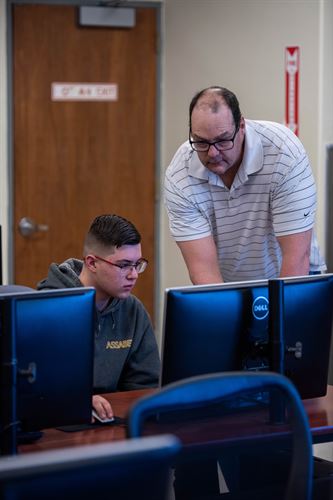 A teacher assisting a student at a computer