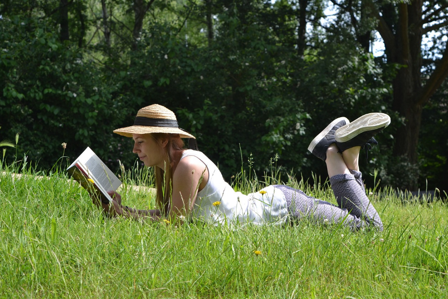 A person reading a book laying in the grass wearing a sun hat