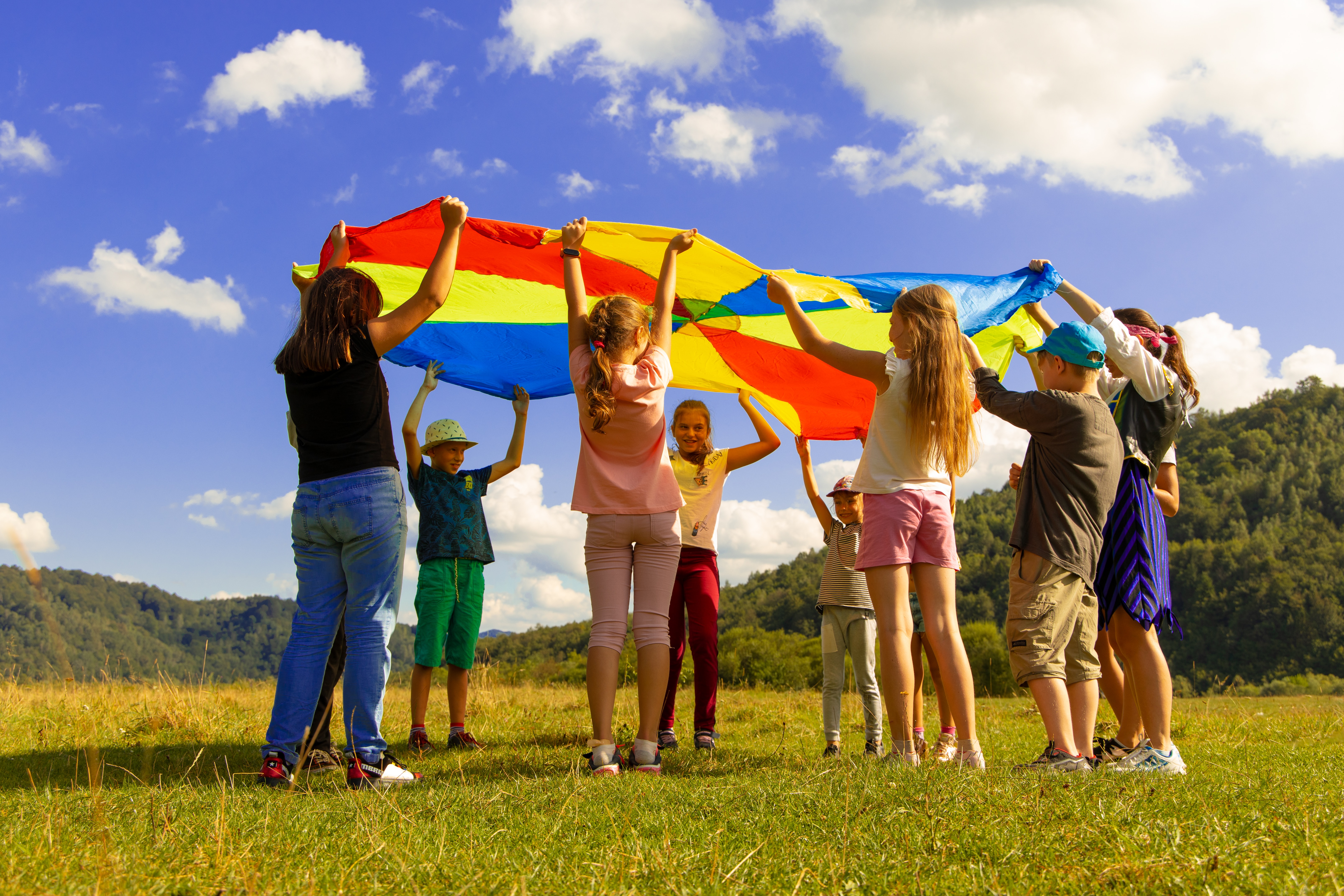Children fluffing a rainbow colored playground parachute in the air