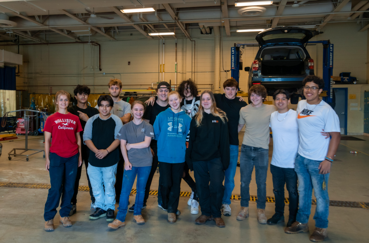 students in a group with a car on a life behind them
