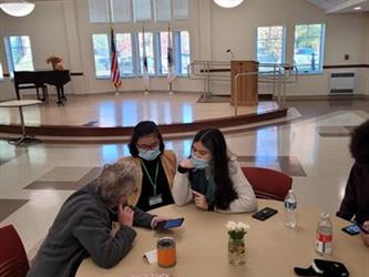 Student helping an adult with their device at a table