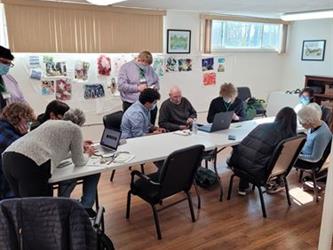 Students around a table helping seniors with their cell phones and computers