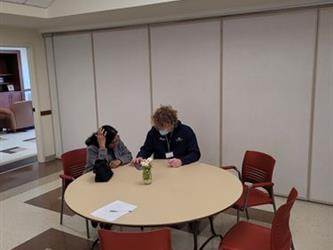 Student helping an adult with their device at a table